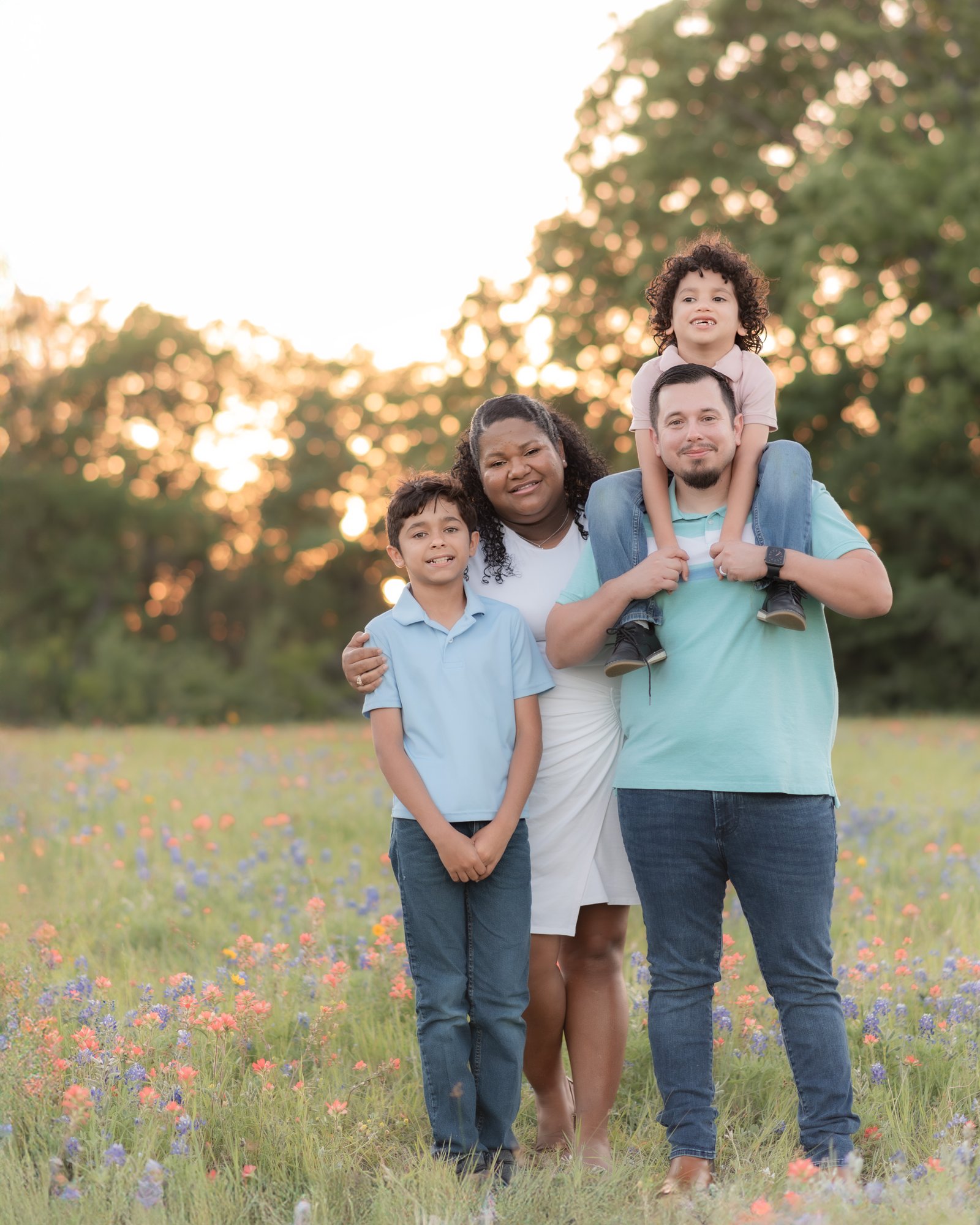 Teresa Vitela bluebonnet family portrait - happy family of four in blue teal and white outfits smiling in Texas bluebonnet field Bryan Texas
