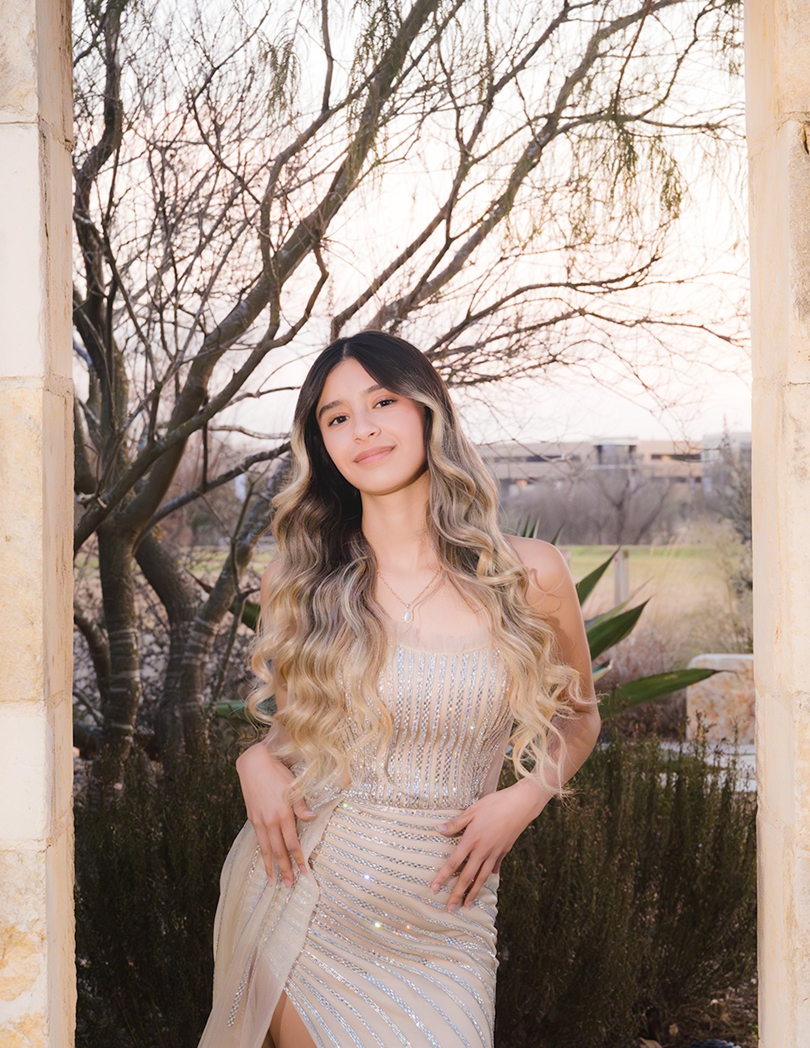 Teresa Vitela luxury senior session - magazine worthy portrait young woman in beige gown emerging through cantera stone door Texas A&M Gardens College Station Texas