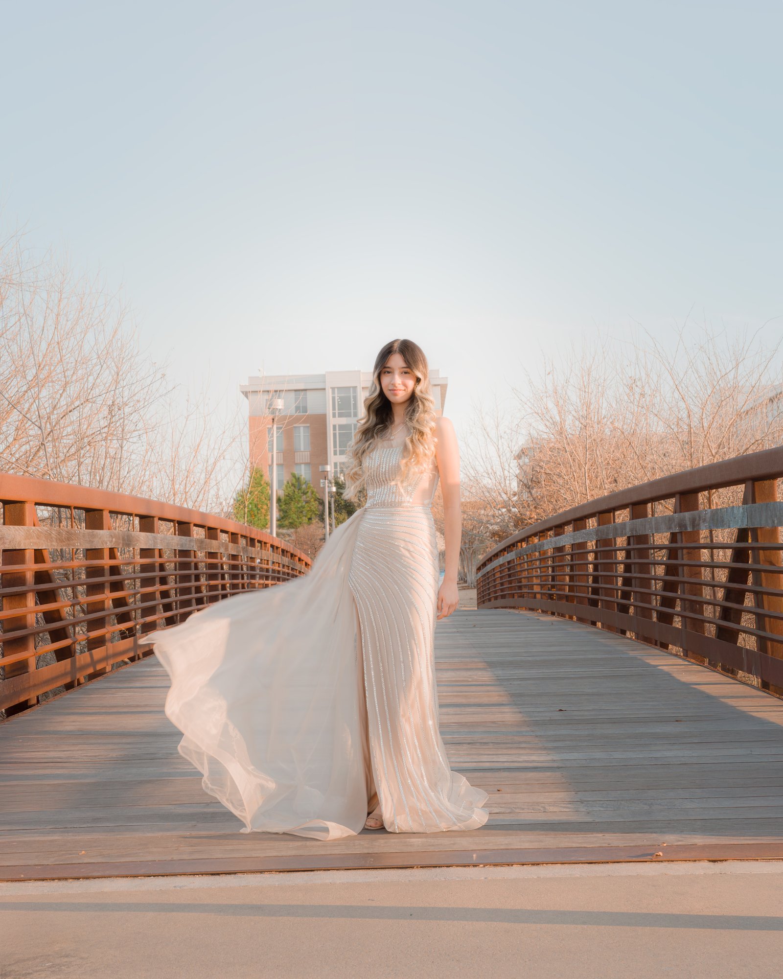 Teresa Vitela senior portrait - elegant young woman in long beige dress posing on bridge Texas A&M Gardens College Station Texas