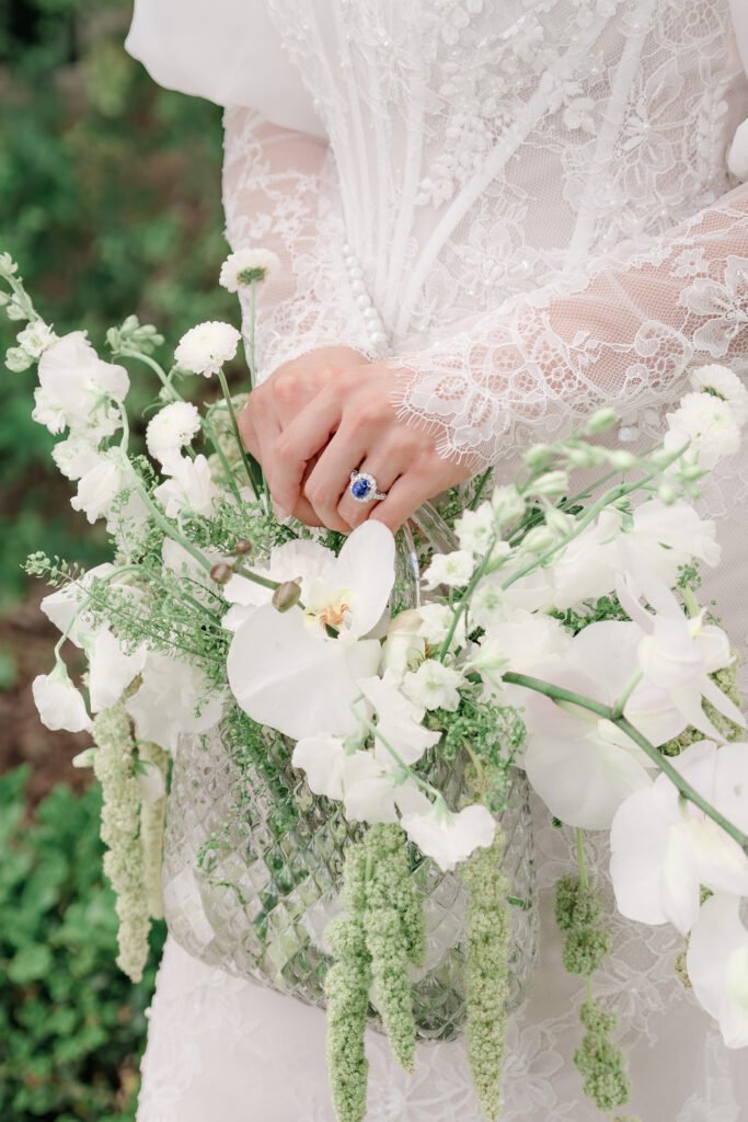 Close up of a bride holding flowers with a luxury sapphire ring and fine art wedding jewelry details.