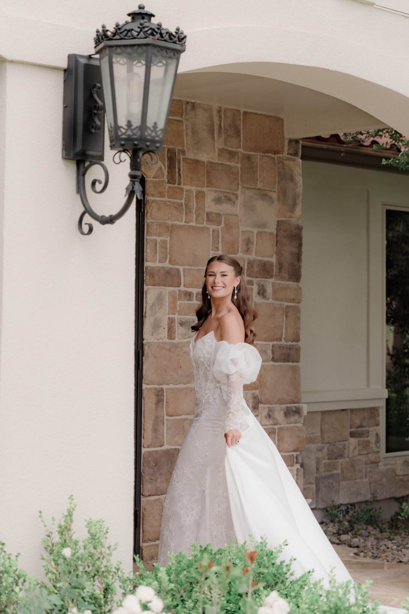Elegant bride posing under a large organic floral installation at a wedding venue.