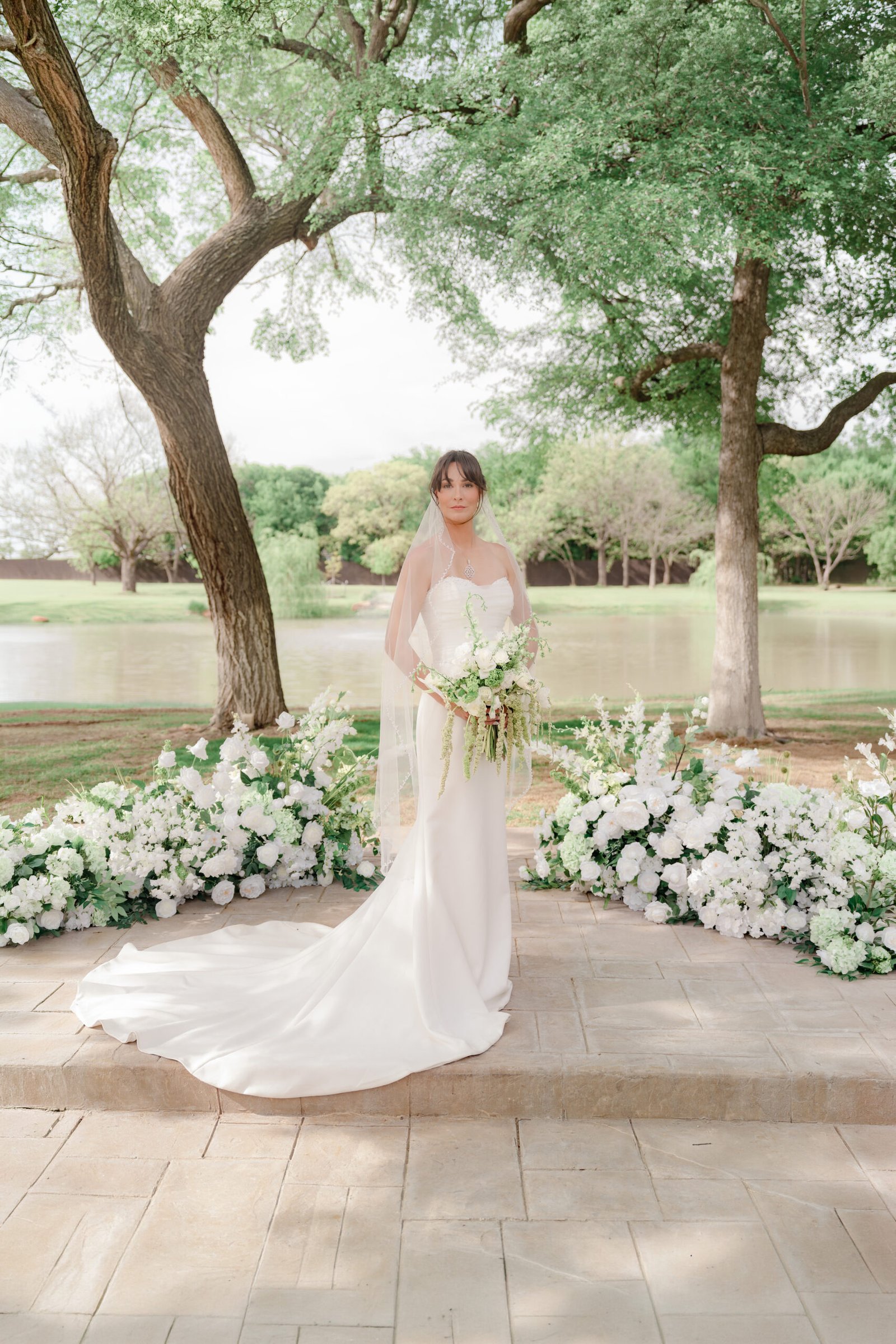 Fine art bridal portrait featuring a luxury wedding dress with a long train and outdoor floral design installation.