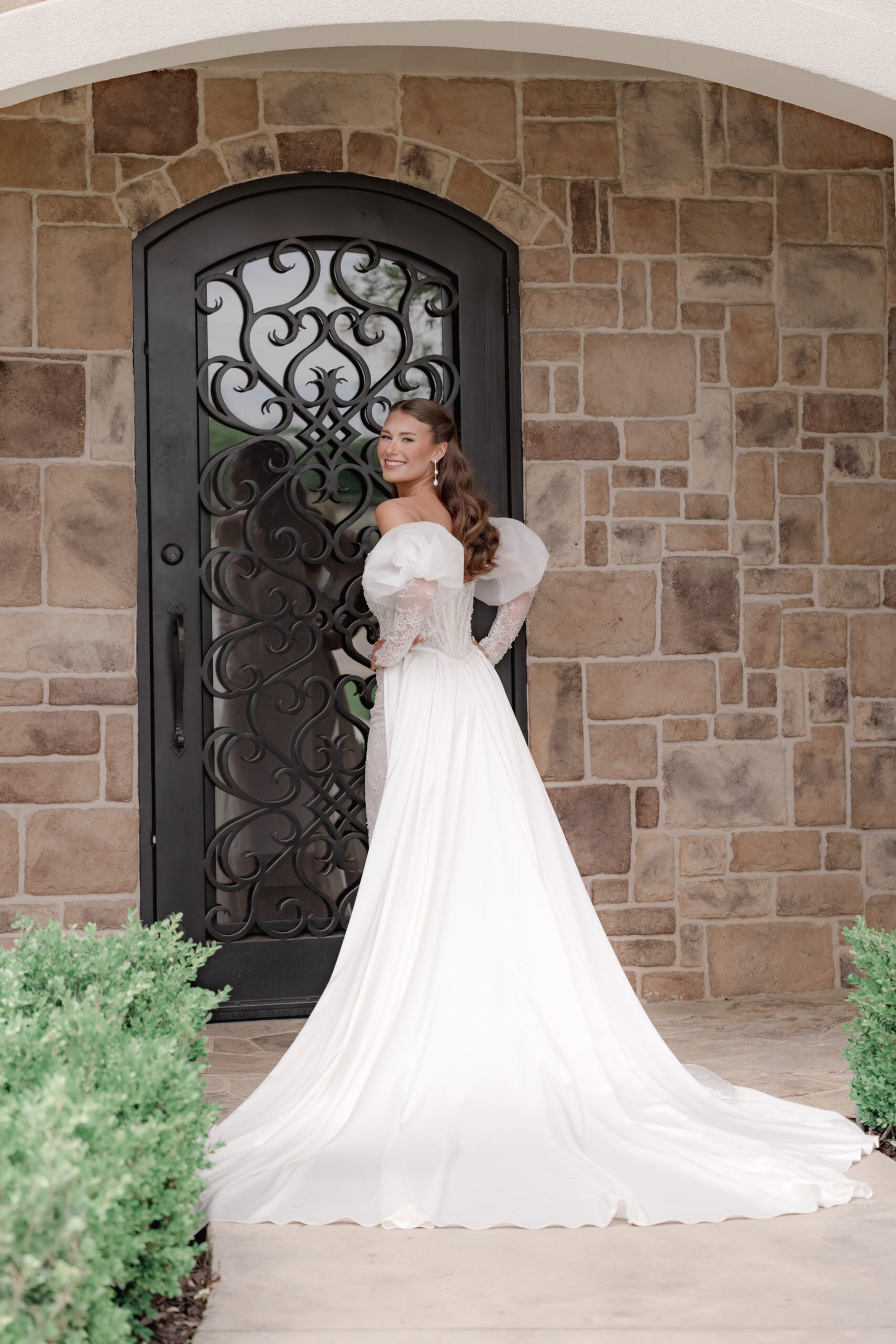 Elegant bride in a high-fashion wedding dress posing in front of a luxury estate arched stone doorway.