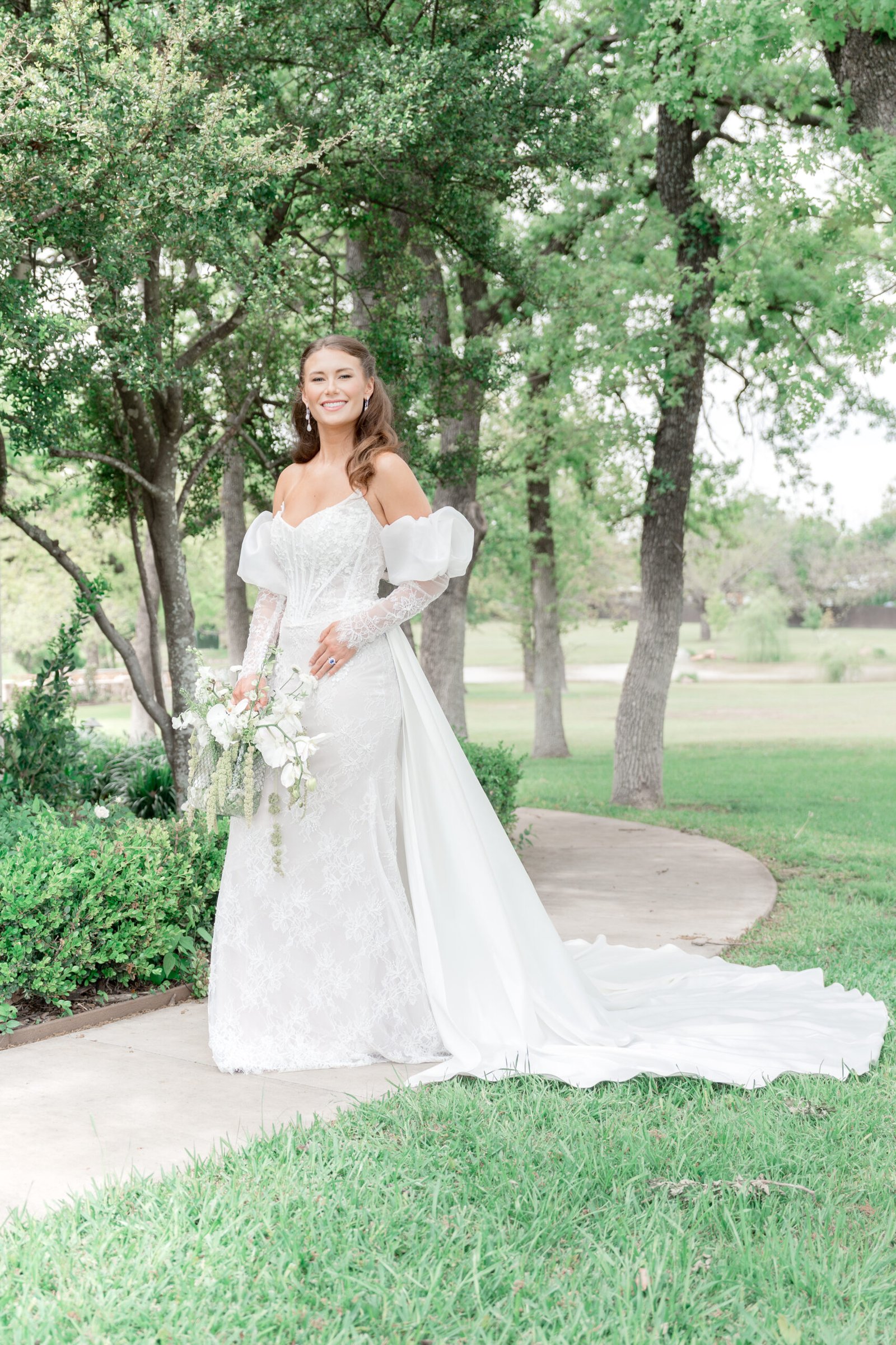 Luxury fine art bride portrait displaying long train wedding dress on curved walkway in College Station TX