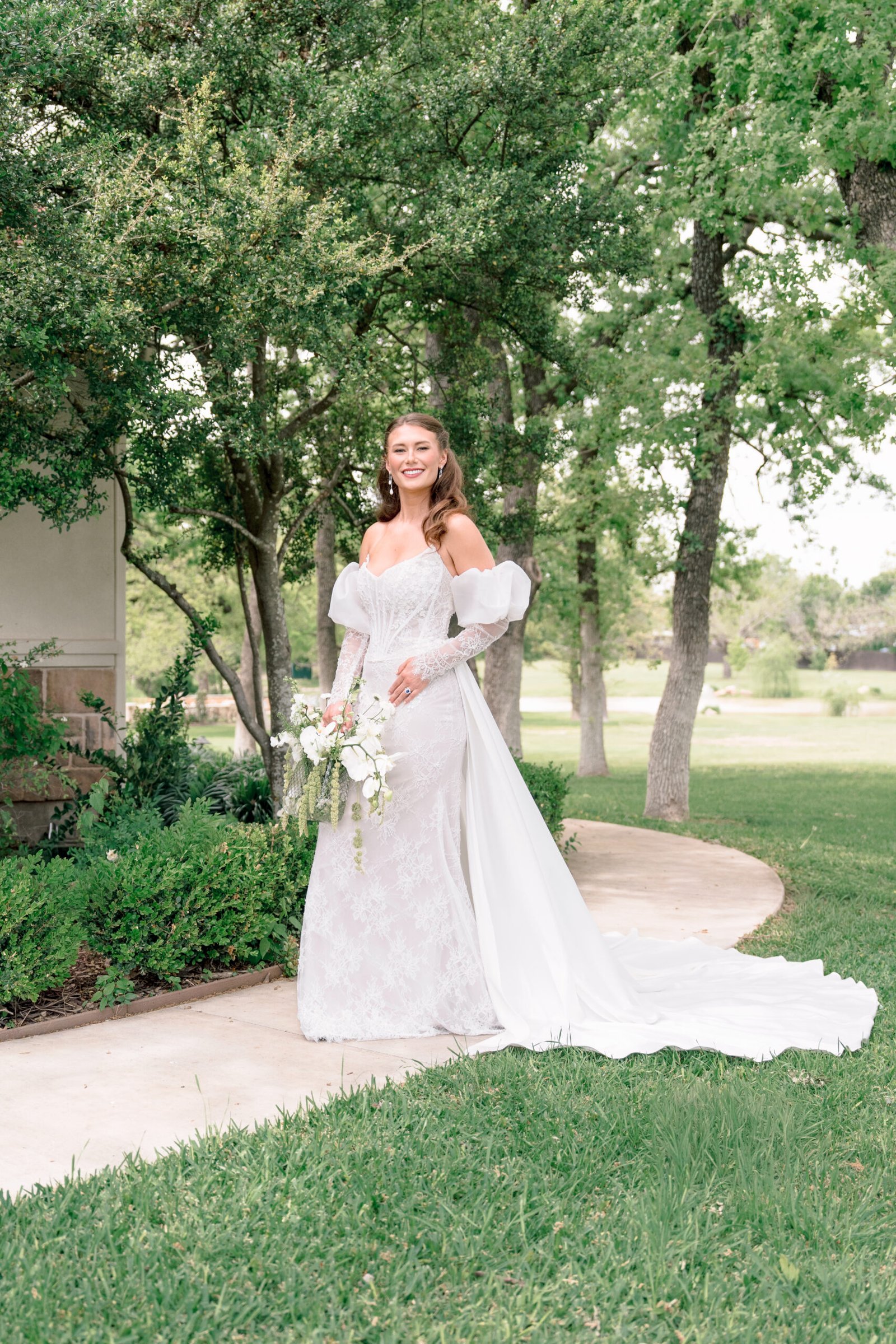 Luxury fine art bride portrait displaying long train wedding dress on curved walkway in College Station TX